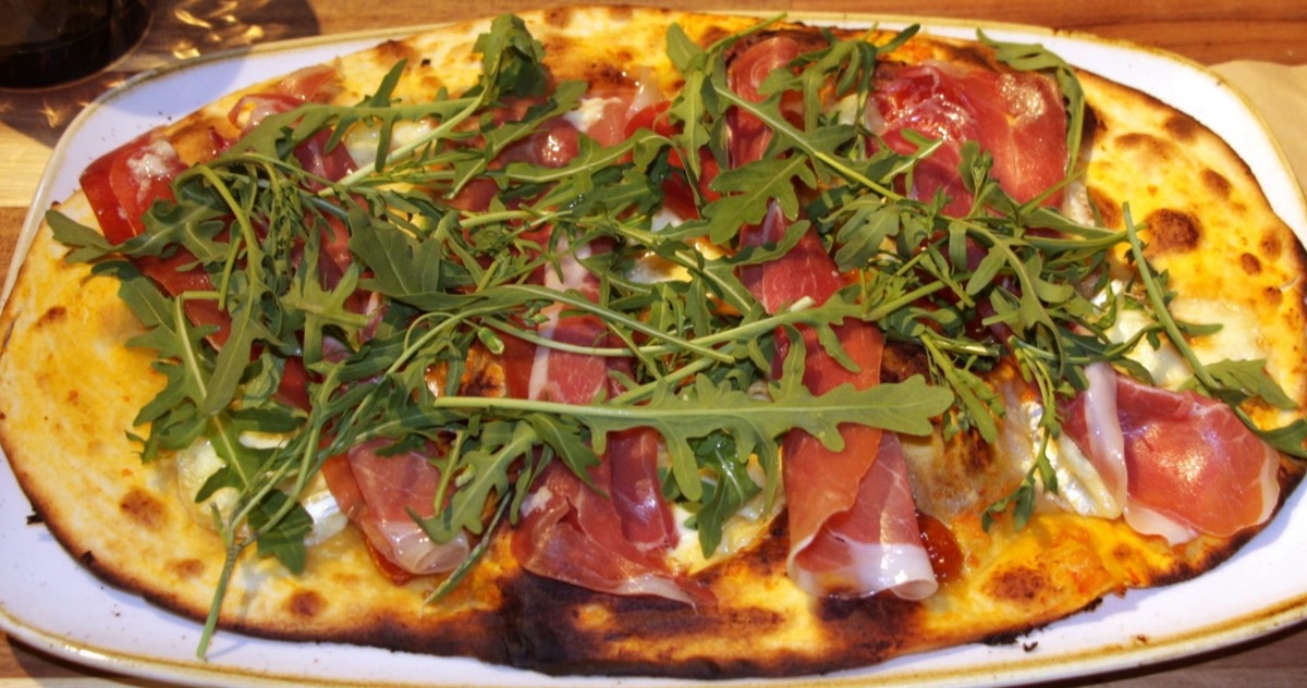 Pizza de Sa Clàssic Blanes amb pernil serrà i ruca, servida en una safata ovalada